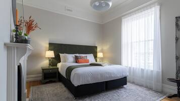 A bedroom with a bed, bedside lamps, a fireplace, and a large window with sheer curtains.