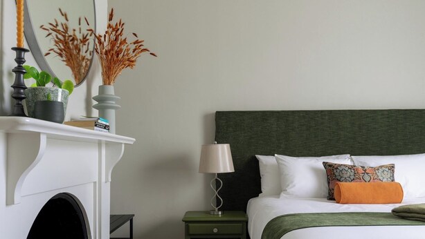 A bedroom with a bed, nightstand, lamp, and a fireplace with decorative items. - Annie May B&B (Devonport)