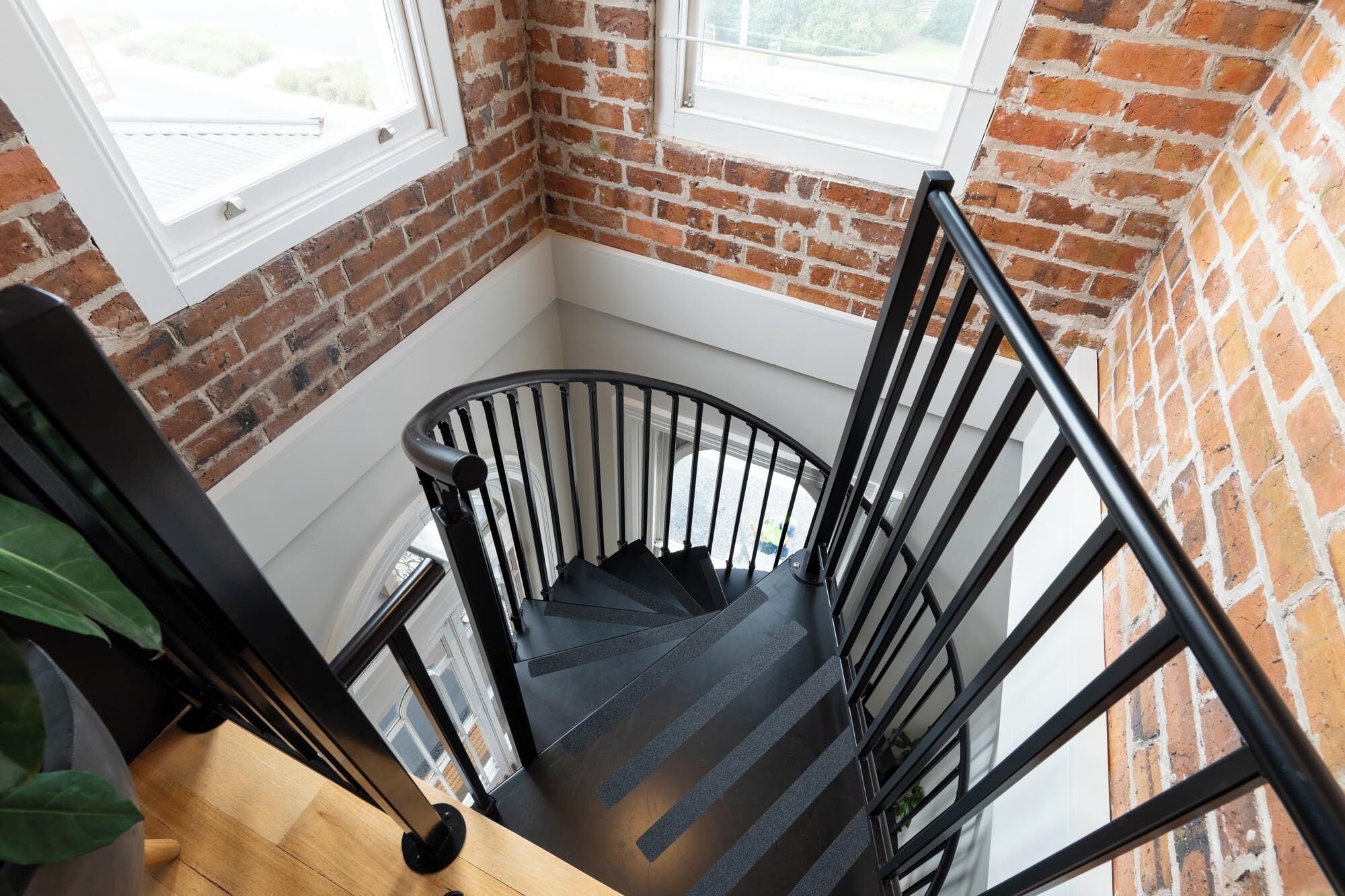 A spiral staircase with black railings in a room with brick walls and a window.