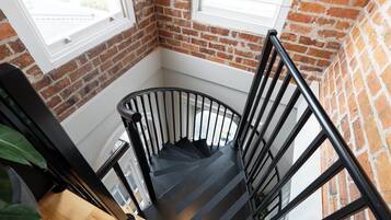 A spiral staircase with black railings in a room with brick walls and a window.