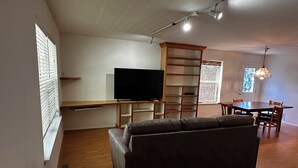 Ein modernes Wohnzimmer mit Flachbildfernseher, einer Couch, einem Esstisch und einer Deckenleuchte.