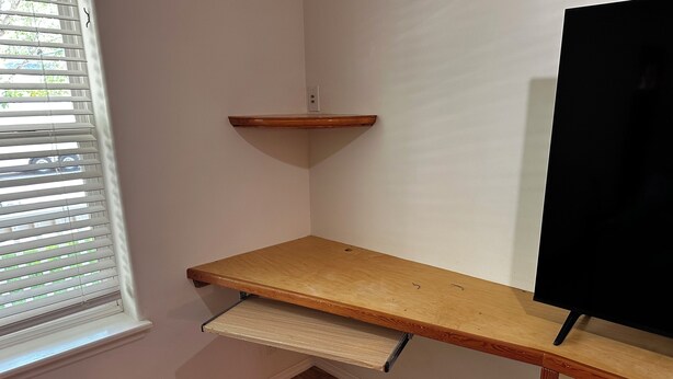 Ein Eckzimmer mit einem Holztisch, einer kleinen Ablage und einem schwarzen TV-Schrank.