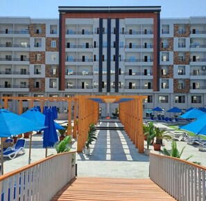 A modern hotel with a central atrium, multiple balconies, and outdoor seating areas. - Serenity Sands Red Sea Hurghada (Red Sea Governorate)