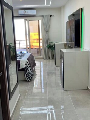 Una habitación de hotel moderna con una cama, un escritorio pequeño, un televisor y una puerta de cristal corredera que da a un balcón.