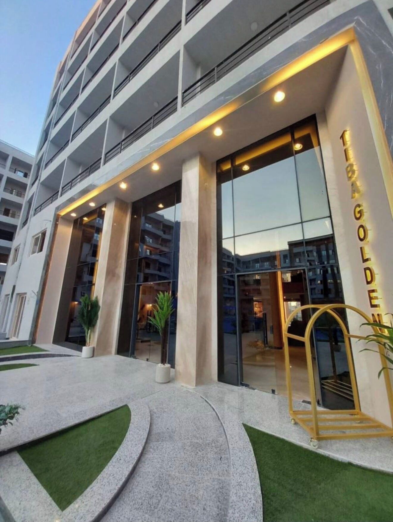 Un hotel de varios pisos con fachada moderna, amplios ventanales de vidrio y una entrada destacada con marco dorado.