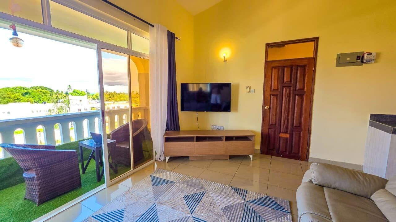Un soggiorno con divano, televisore e un balcone con mobili da esterno.