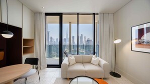 A modern hotel room with a sofa, a dining table, and a view of a city skyline. - Executive Studio w Burj Khalifa View (Dubai)