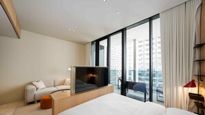 A modern hotel room with a large bed, a sofa, a TV, and a view of the cityscape through floor-to-ceiling windows. - Urban Upside Studio Near Downtown (Dubai)
