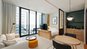 A modern hotel room with a sofa, a round table, a TV, a balcony with a view of the city, and a kitchenette. - Urban Upside Studio Near Downtown (Dubai)