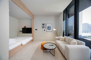 Ein modernes Hotelzimmer mit einem Bett, einer Couch, einem kleinen Tisch und einem großen Fenster mit Blick auf die Stadt.