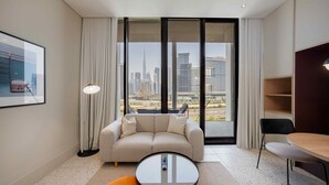 Ein modernes Hotelzimmer mit einer Sitzecke, einem kleinen runden Tisch, einem Sessel und einem großen Fenster mit Blick auf die Stadt.