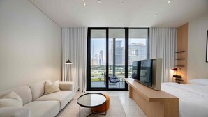 A modern hotel room with a sofa, a round coffee table, a TV, and a bed. - Sleek Studio w Burj Khalifa View (Dubai)