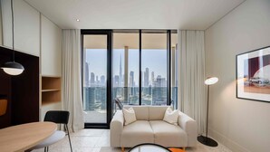 Ein modernes Hotelzimmer mit Sofa, Esstisch, Stuhl, Stehlampe und Blick auf die Skyline der Stadt.
