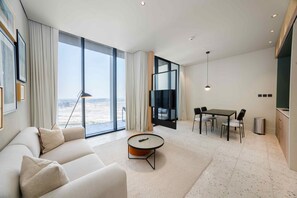 A modern living room with a sofa, a coffee table, a dining area with a table and chairs, a TV, and large windows offering a view. - Prime Upside Studio w Private Balcony (Dubai)
