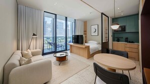Ett modernt hotellrum med en balkong, en soffa, en säng, ett skrivbord och en matplats.