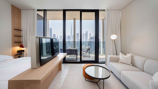 A modern hotel room with a large bed, a TV, a sofa, and a balcony with a city view. - Bright Studio w Iconic Burj View (Dubai)