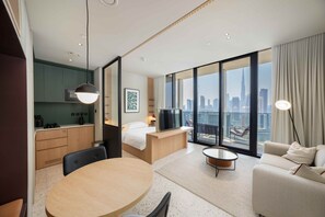 A modern hotel room with a dining area, a bed, a TV, and a city view. - Bright Studio w Iconic Burj View (Dubai)