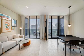 Ein modernes Wohnzimmer mit Sofa, Couchtisch, Esstisch und Stühlen. Große Fenster bieten Blick auf die Stadt.