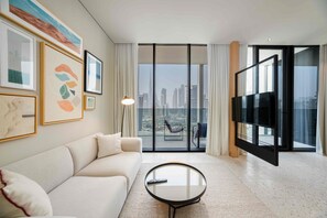Ein modernes Wohnzimmer mit Sofa, Couchtisch, Fernseher und Blick auf eine Stadtlandschaft durch große Fenster.