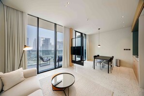 A modern hotel room with a large balcony, a dining area, and a flat-screen TV.