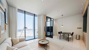 A modern living room with a sofa, a coffee table, a dining area with chairs, a TV, and a view of the cityscape. - Upscale Business Bay Studio w Pool (Dubai)