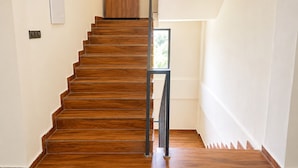 Eine Holztreppe mit Handlauf, die zu einer Zwischenebene mit Tür und Fenster führt.