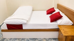 Ein Bett mit weißer Bettwäsche und roten Kissen, ein Holz-Kopfbrett und ein Nachttisch mit Schubladen.