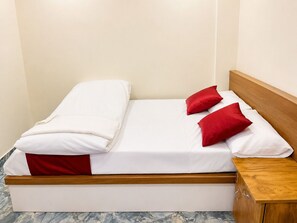 A bed with white bedding and red pillows, a wooden headboard, and a wooden nightstand with drawers. - Vilstay Go Malabar Comfort Rooms  (Ambalapuzha)