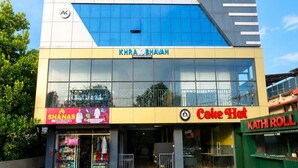 Ein mehrgeschossiges Geschäftsgebäude mit Schildern für 'AK BUILDING', 'KHRA BHAVAN', 'SHANAS', 'Cake Hat' und 'KATHI ROLL'.