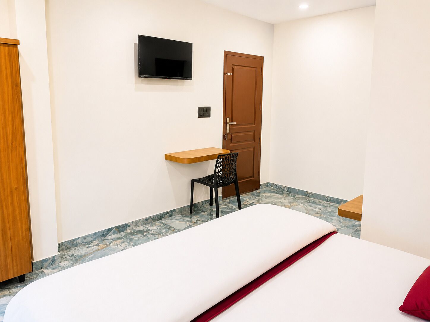 Habitación de hotel con cama, escritorio, silla, televisor montado en la pared y puerta.