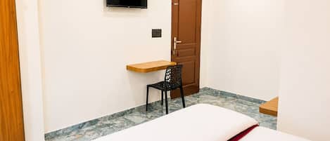 Habitación de hotel con cama, escritorio, silla, televisor montado en la pared y puerta.
