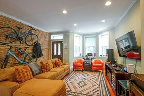 Ein Wohnzimmer mit Backsteinwand, einer Couch, einem Couchtisch, zwei Sesseln, einem Fernseher und einem Fahrrad.