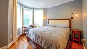 A bedroom with a large bed, a nightstand, a desk, and a window with curtains. - Quiet Home in Walkable Area: 3 Mi to National Mall (Washington)