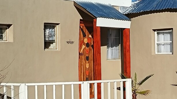 A house with a white fence, a wooden door, and a small window. - Room-11 on High Airbnb za (Gariep)