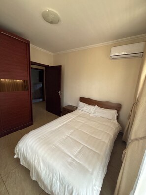 A hotel room with a bed, a wooden wardrobe, a nightstand, and an air conditioning unit.