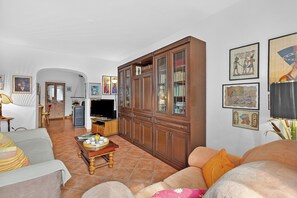 Ein Wohnzimmer mit einer Couch, einem Fernseher, einem Schrank und gerahmten Bildern an der Wand.