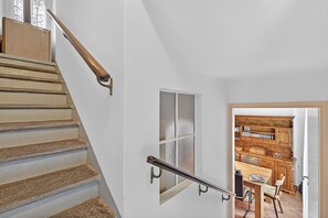 Eine Treppe mit Metallgeländer, eine Holztür zu einer Küche mit Holzausstattung und einem Esstisch.