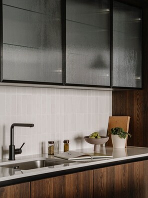 A kitchen with a modern faucet, a white tiled backsplash, and wooden cabinets. - Fulham Residences Two (London)