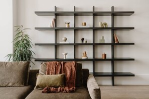 Ein modernes Wohnzimmer mit einer dunkelholzene Regaleinheit an einer schlichten Wand, einem braunen Sofa mit Kissen und einer grünen Pflanze.