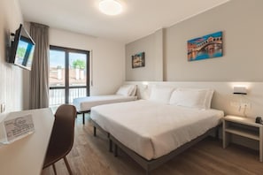 Hotellihuone, jossa on kaksi sänkyä, työpöytä, tuoli, televisio ja taideteoksia seinillä.