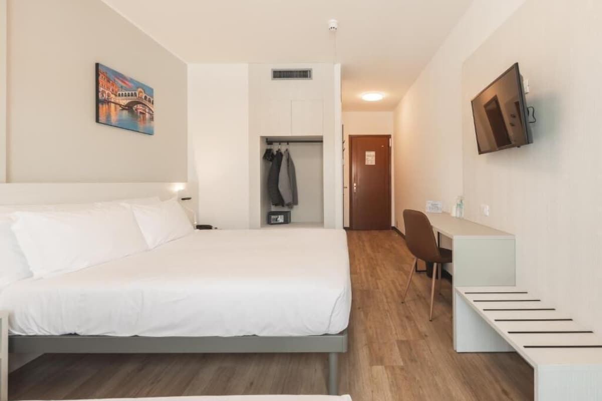 Hotellihuone, jossa on sänky, työpöytä, tuoli, televisio ja taulu seinällä.