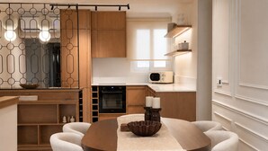 A modern kitchen with wooden cabinets, a built-in oven, a microwave, and a dining area with a round table and six chairs. - Meros Marotti | Spacious 3BR Home in Zakynthos (Zakinthos)