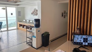 A hotel reception area with a computer monitor displaying multiple camera feeds, a water dispenser, a trash bin, and a wooden partition. - The Palm Aryan Mussoorie 5min Mall Road (Mussoorie)