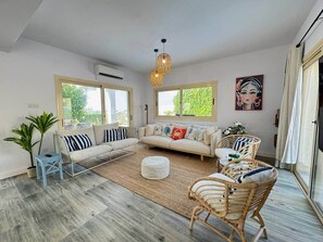A modern living room with a sofa, chairs, a coffee table, and a large window. - Anthorina Villa 3 Protaras - walk to beach (Paralimni)