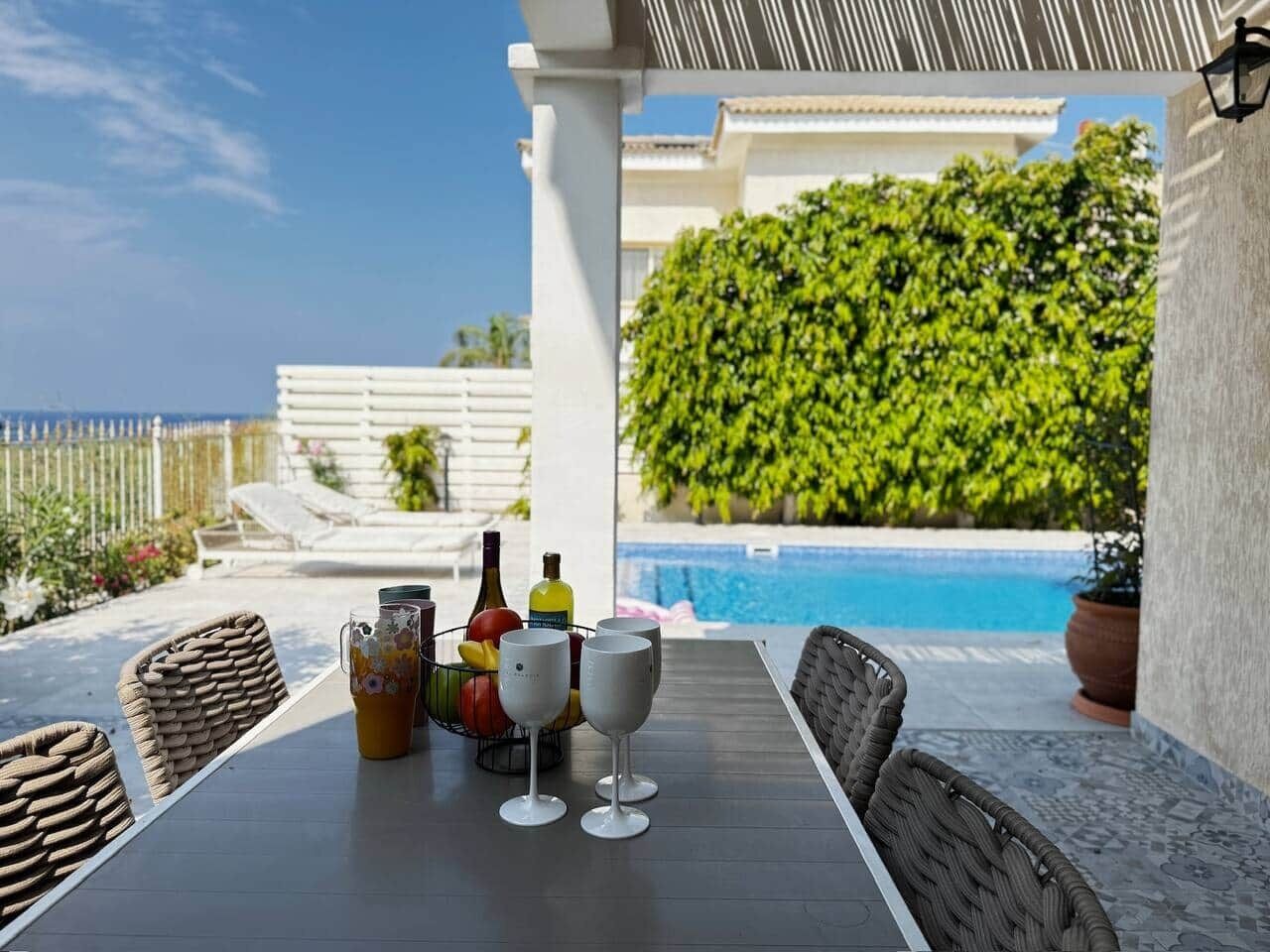 Un espace extérieur aménagé pour les repas, avec une piscine, des meubles en osier et une table dressée avec des verres et des bouteilles de vin.