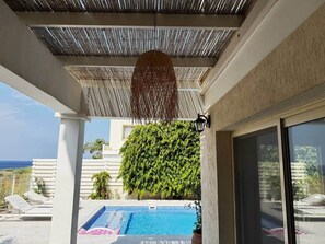 A pool area with a view of the sea, a covered patio, and a large green bush. - Anthorina Villa 3 Protaras - walk to beach (Paralimni)