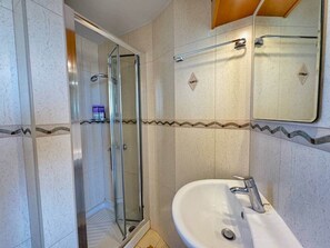 Un baño con cabina de ducha de vidrio, un lavamanos blanco y un espejo encima.