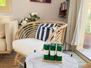 A wicker chair with a striped pillow, a round table with green bottles, and a sofa in a room with a view. - Anthorina Villa 3 Protaras - walk to beach (Paralimni)