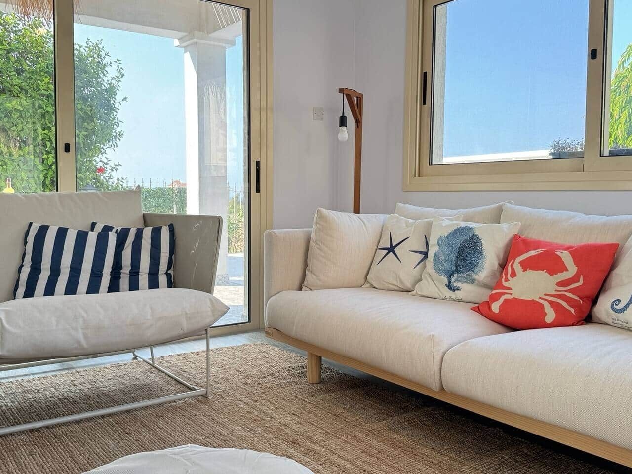 A modern living room with a sofa and armchair, a large window, and a floor lamp.