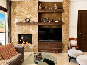 A living room with a fireplace, television, and a coffee table with decorative items. - Emerald Seafront Residence (Sotira)